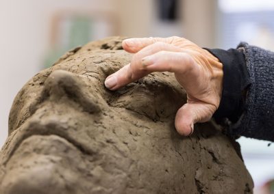 Maïté Duval werkt met haar hand het oog van een beeld in klei bij